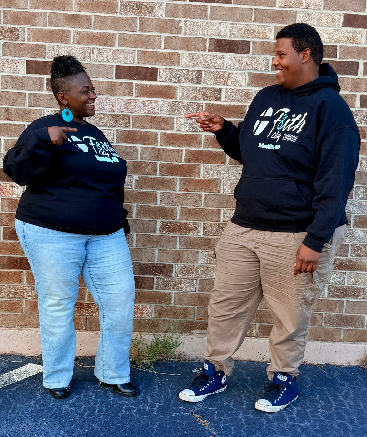 Two church members in a F8ith City sweatshirt and hoodie, pointing at each other and laughing