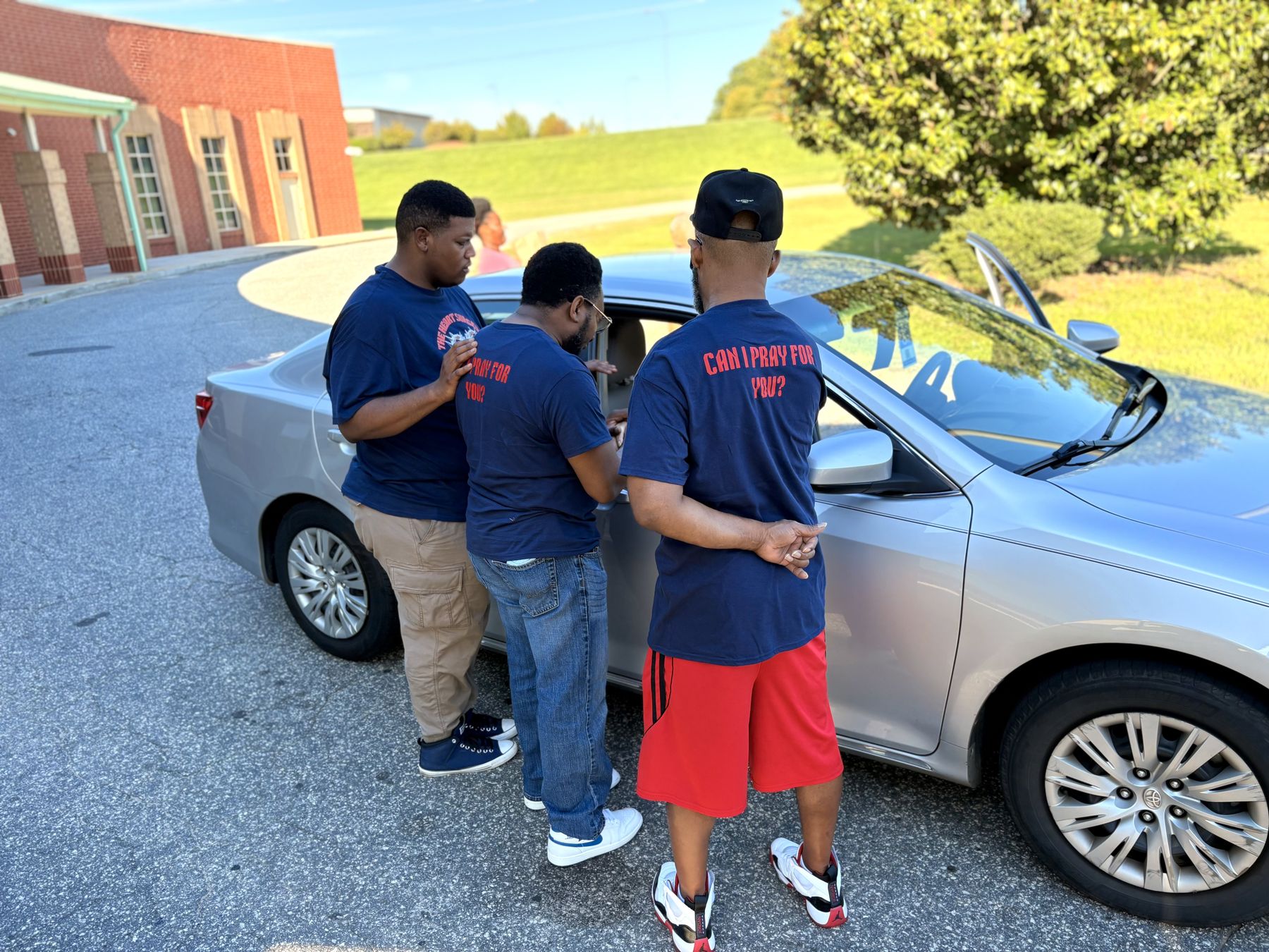 Volunteers praying with a neighbor beside a car